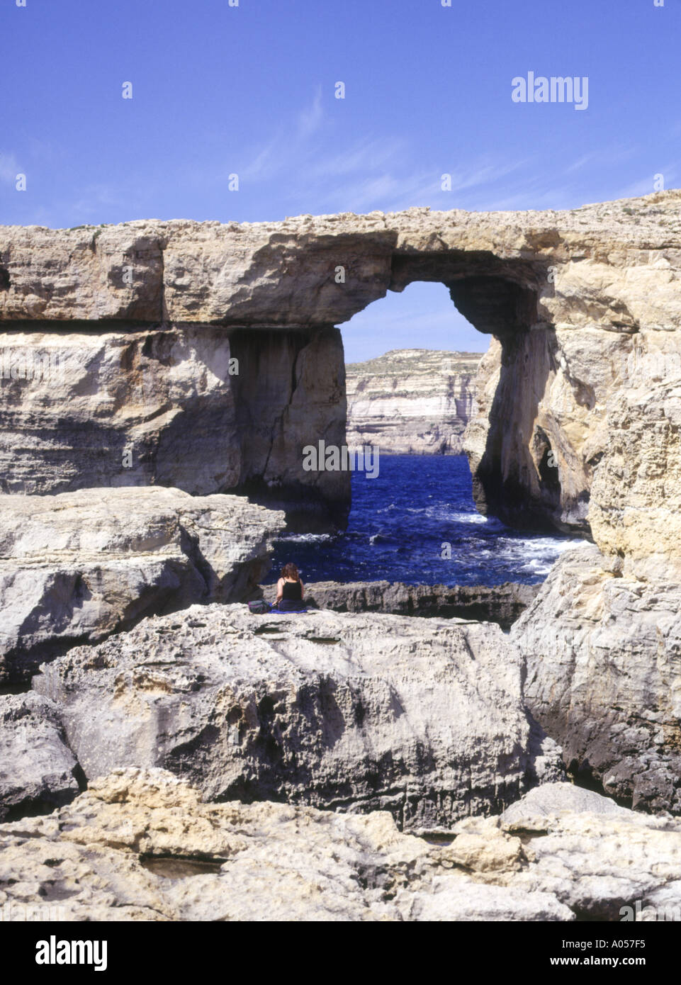 Fenêtre d'Azur dh POINT DWEJRA GOZO Girl sitting on rock à la roche naturelle au passage de la mer Banque D'Images