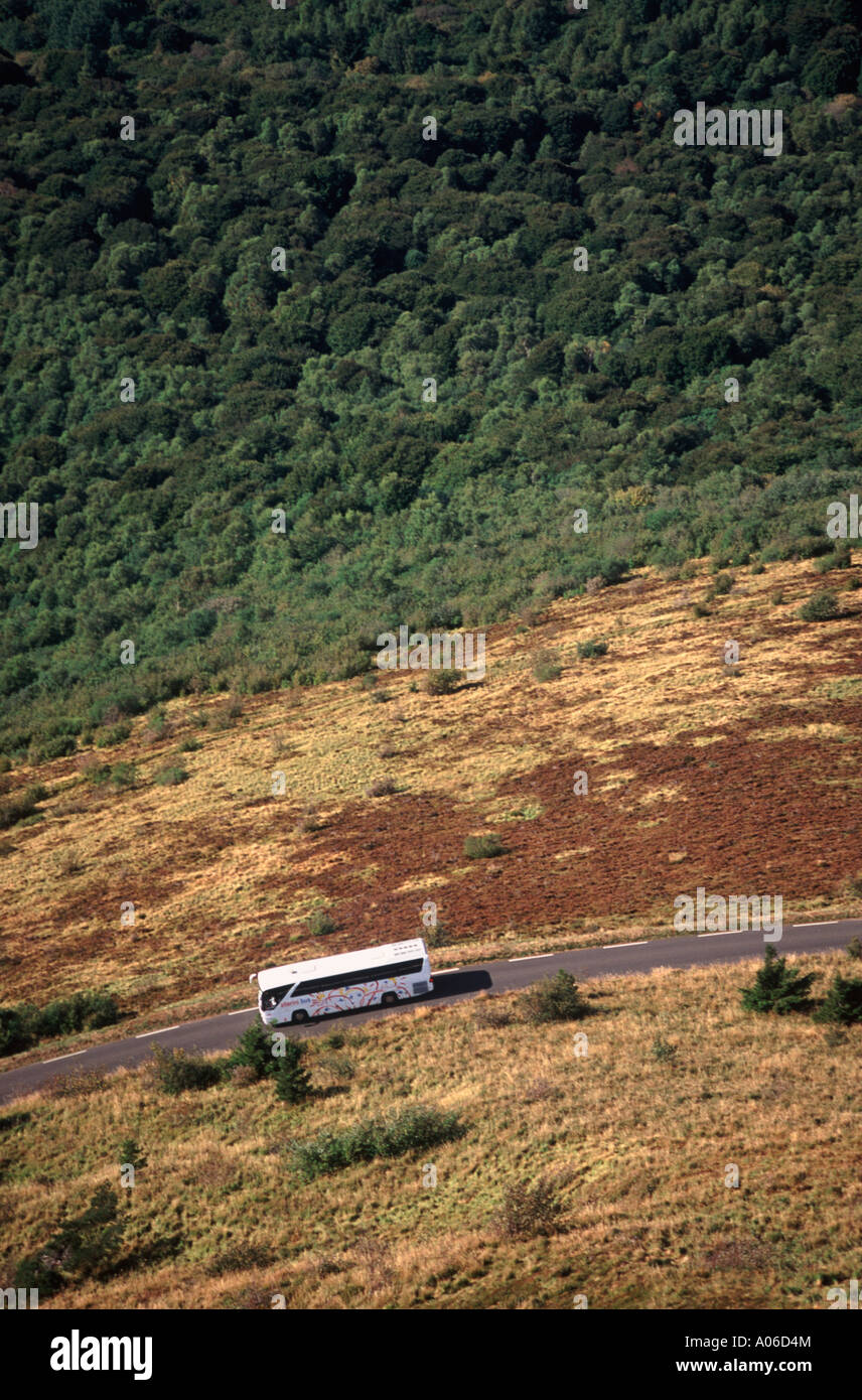 TOUR BUS roulant sur route à travers des courbes du paysage volcanique ci-dessous Puy de Dôme (près de Clermont-Ferrand), France Banque D'Images