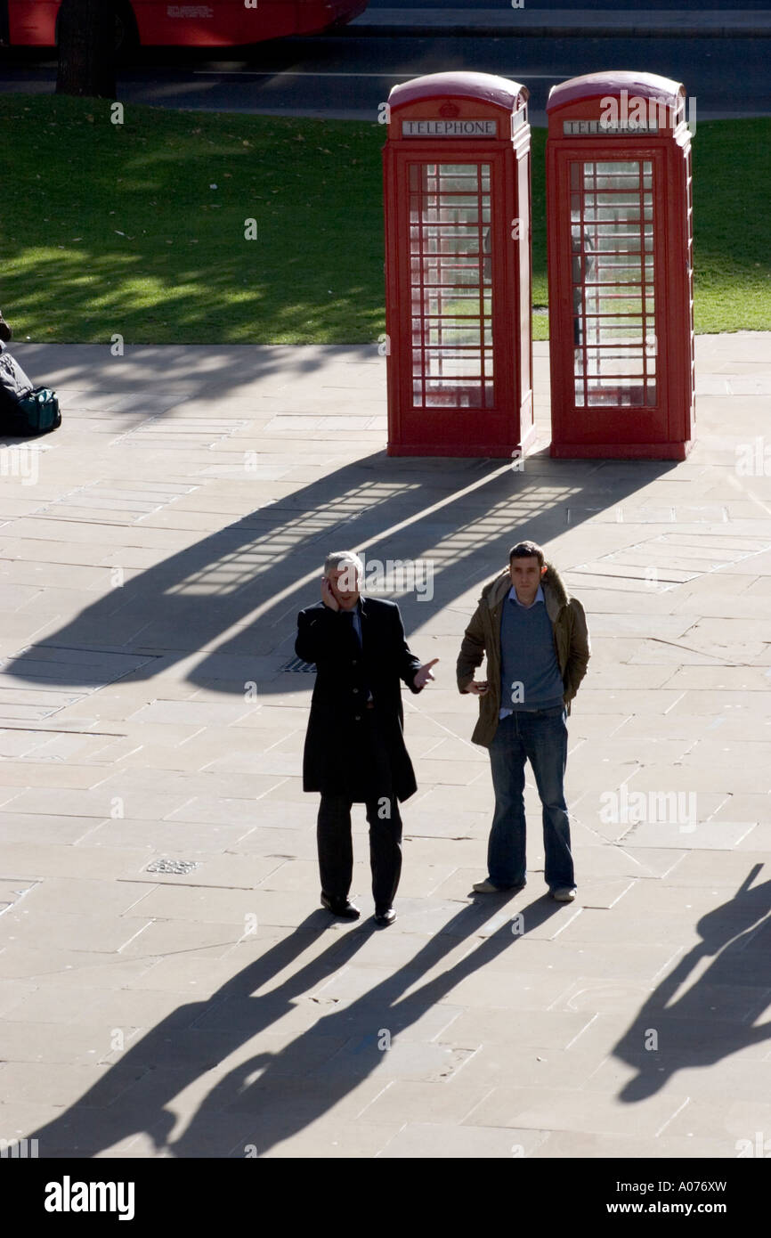 Red Phone box kiosques téléphoniques à la ville de Londres avec un homme sur le téléphone mobile debout dans l'ombre Banque D'Images