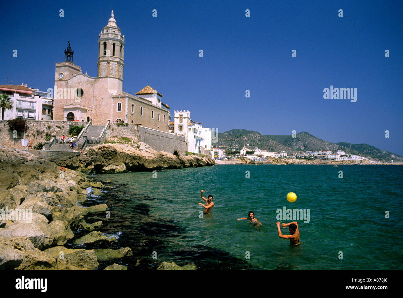 Les jeunes jouent dans la mer en face d'une église catholique à Sitges, Espagne. Banque D'Images