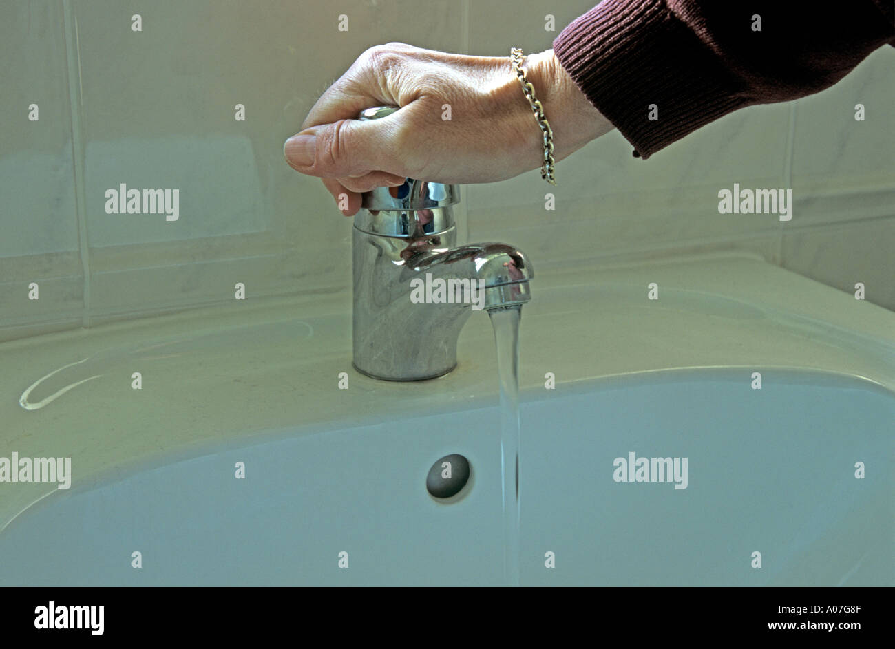 La vie de femme mature encore part d'allumer le robinet mélangeur de lavabo Banque D'Images