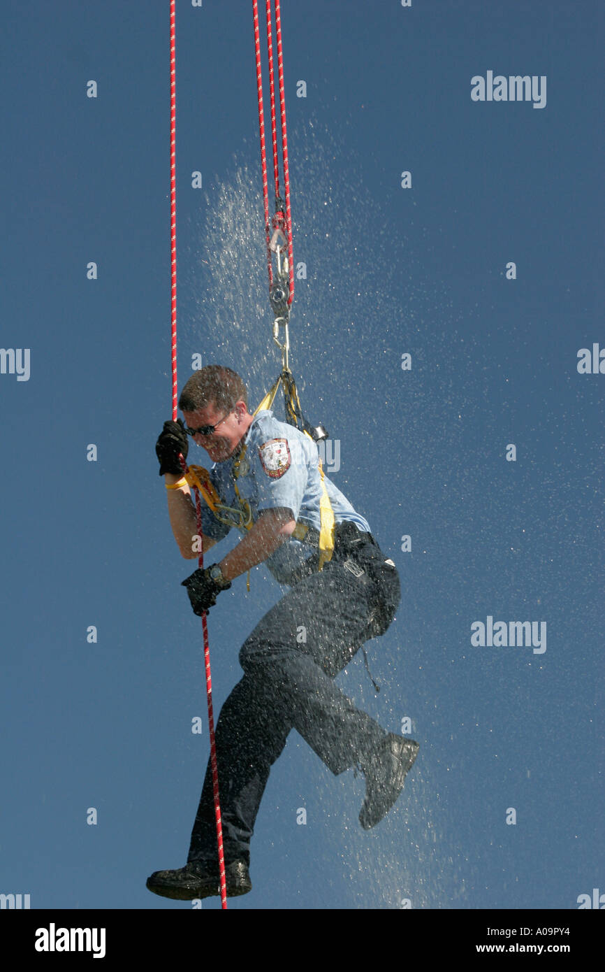 Un pompier est en train de faire l'antenne des cordes et pour le plaisir de ses coéquipiers lui pulvériser de l'eau ci-dessous d'un hoseline Banque D'Images