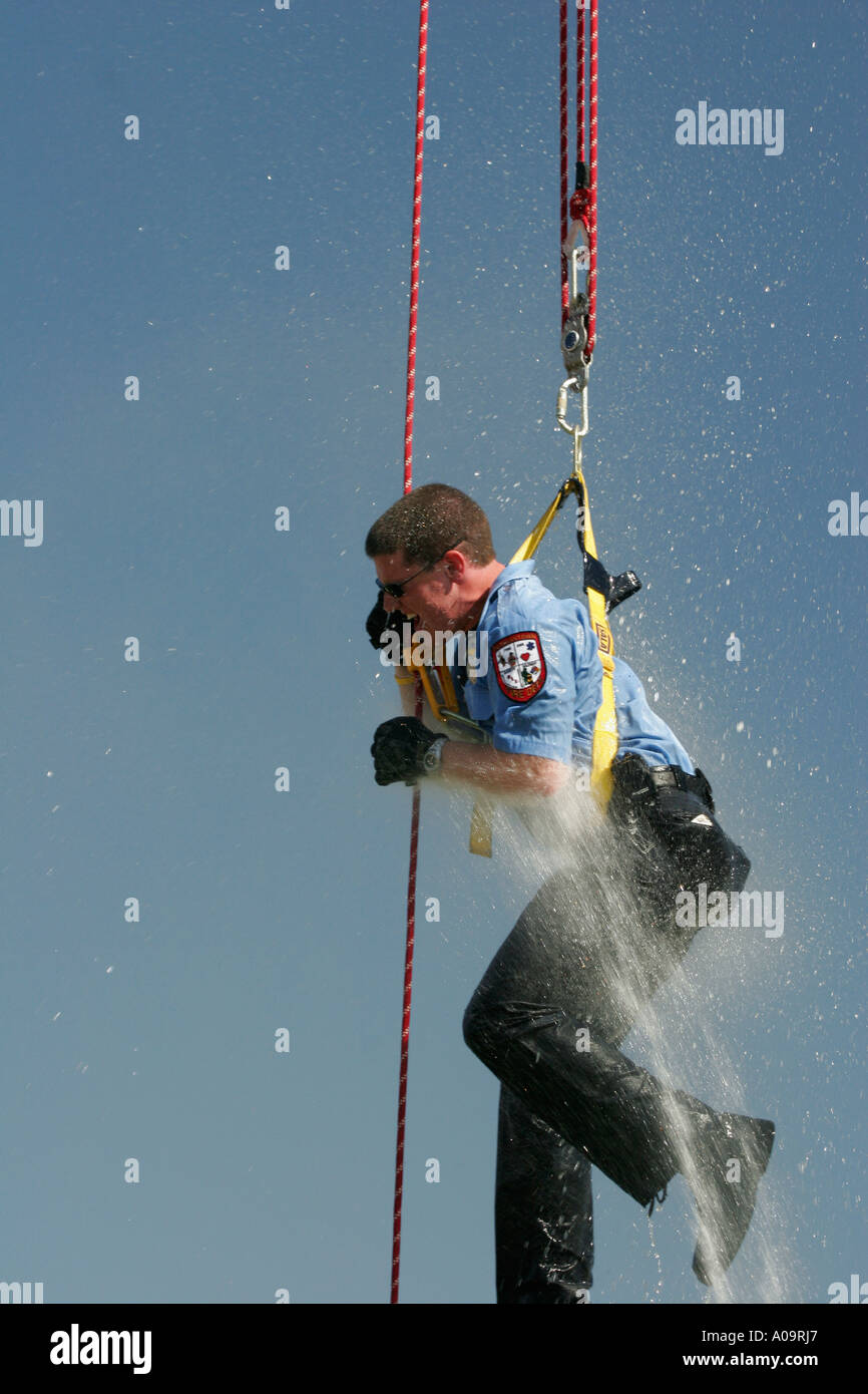 Un pompier est en train de faire l'antenne des cordes et pour le plaisir de ses coéquipiers lui pulvériser de l'eau ci-dessous d'un hoseline Banque D'Images