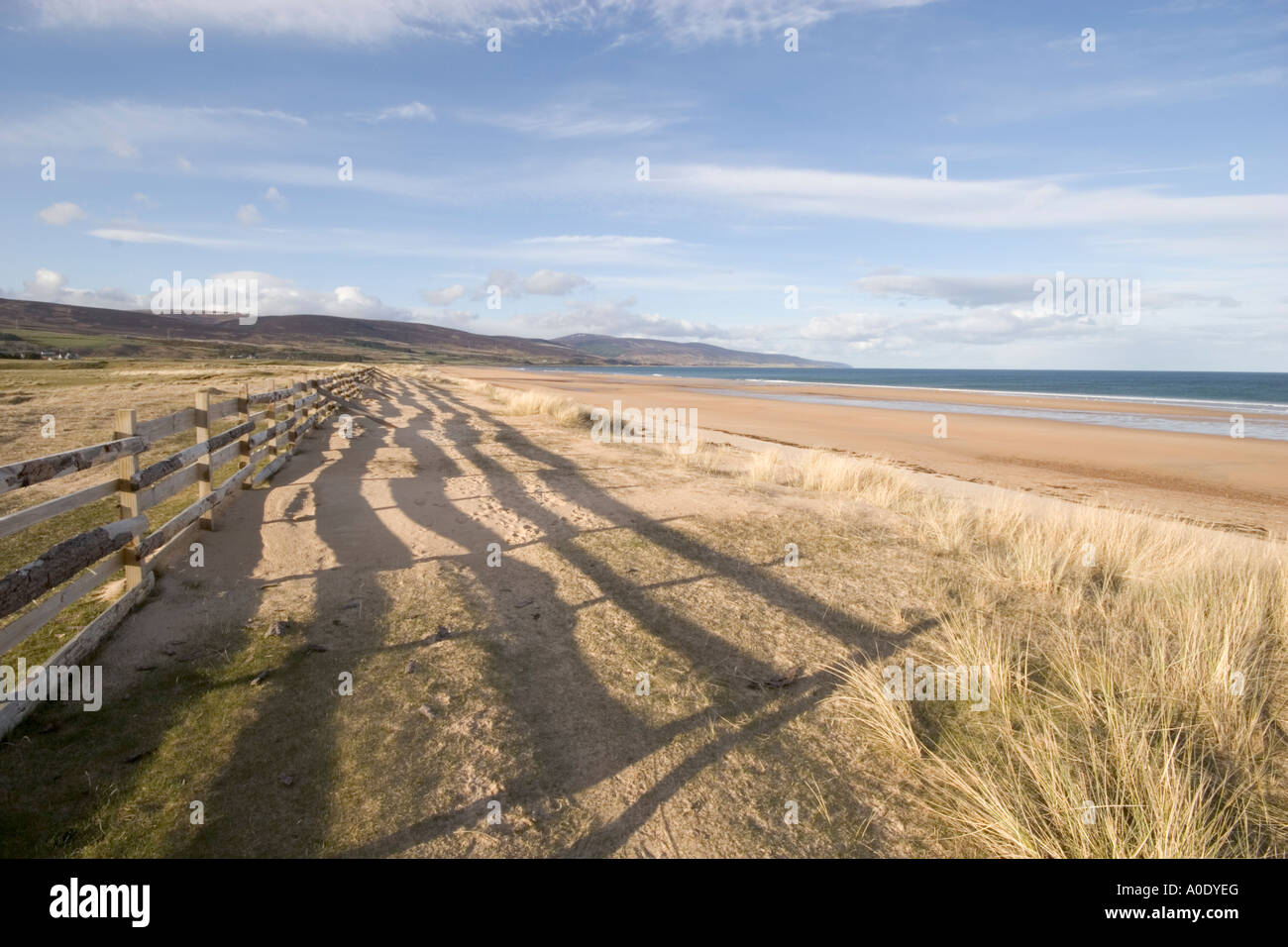 Scène de plage de sable déserte avec CIEL BLEU AVEC DES OMBRES ET CLÔTURE LE LONG DE DUNES DE SABLE Banque D'Images