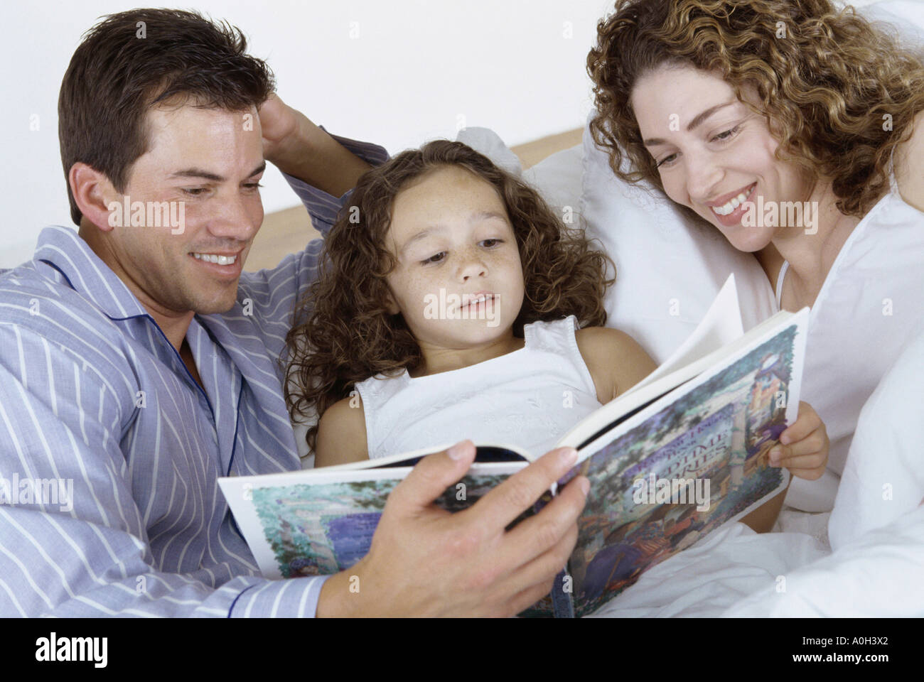 Les parents et leur fille au lit ensemble la lecture d'un livre Banque D'Images