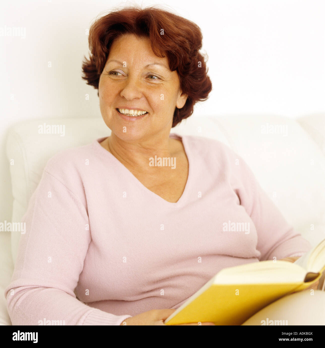 Smiling woman sitting on sofa with book Banque D'Images