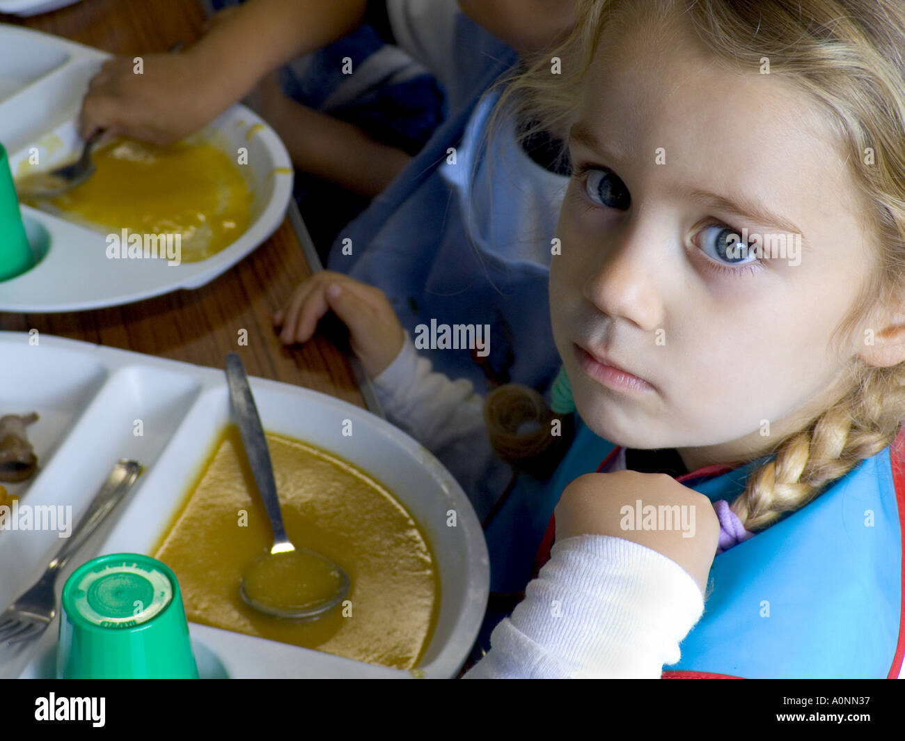 DÎNERS SCOLAIRES PENSIVE APPRÉHENSION TRISTE MALHEUREUSE PLAQUE DE VISAGE ENFANT maternelle BÉBÉ fille blonde avec son repas scolaire intact à la cantine Banque D'Images