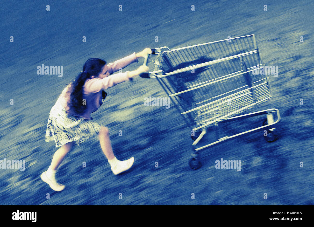 Jeune fille poussant un chariot vide de shopping, à l'extérieur à vitesse en haut d'une colline. Banque D'Images