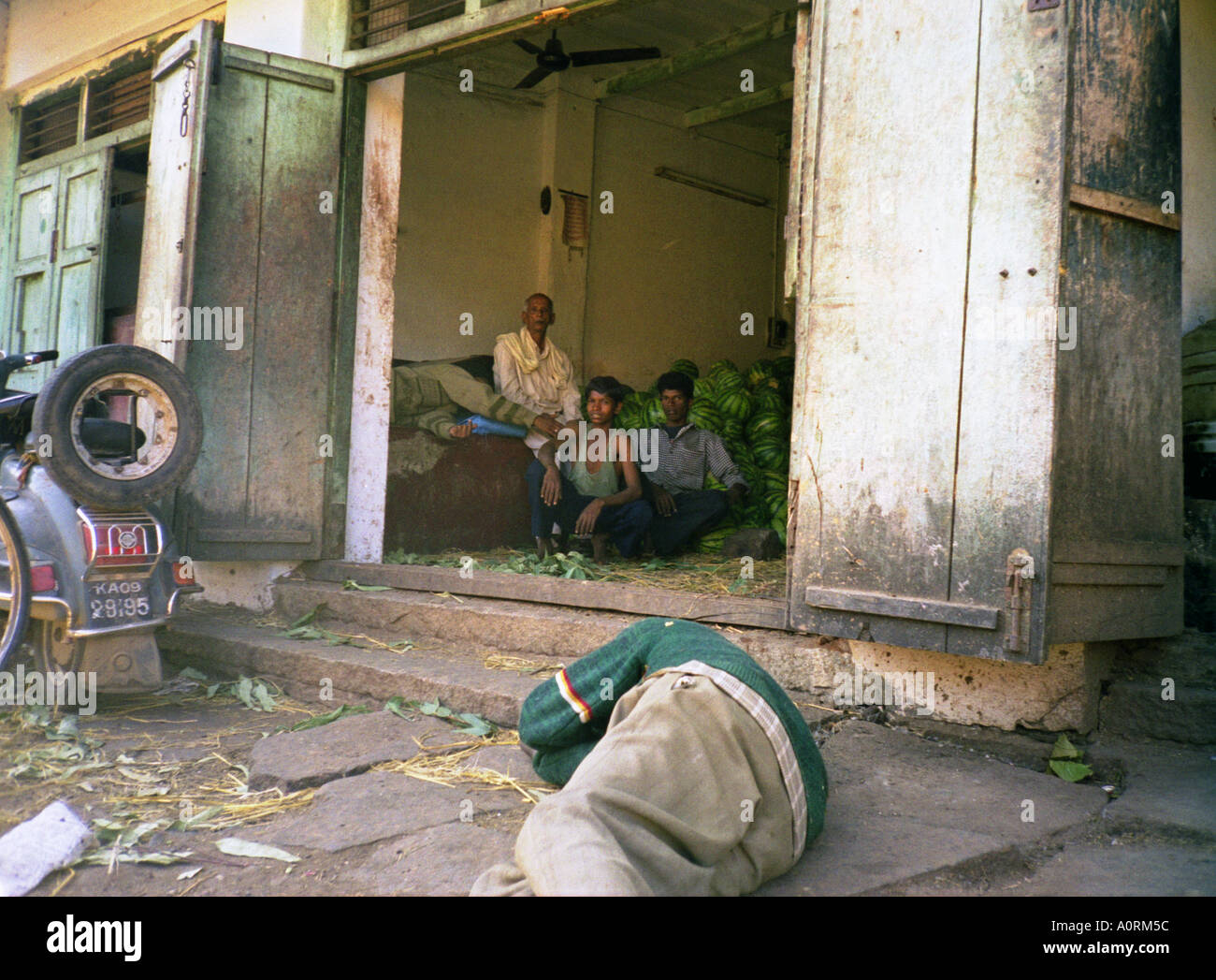 Père Fils groupe homme garçon vendre pastèque & mendiant dormir sur le plancher sale au marché local Mysore Karnataka Inde Asie du Sud Banque D'Images