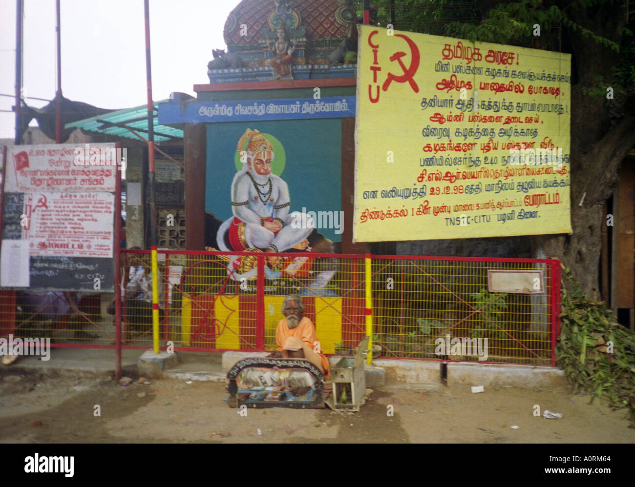 Barbe blanche sage sénile de l'homme hindou typique en vêtements colorés siéger par grand signe communiste Palani Tamil Nadu Inde Asie du Sud Banque D'Images