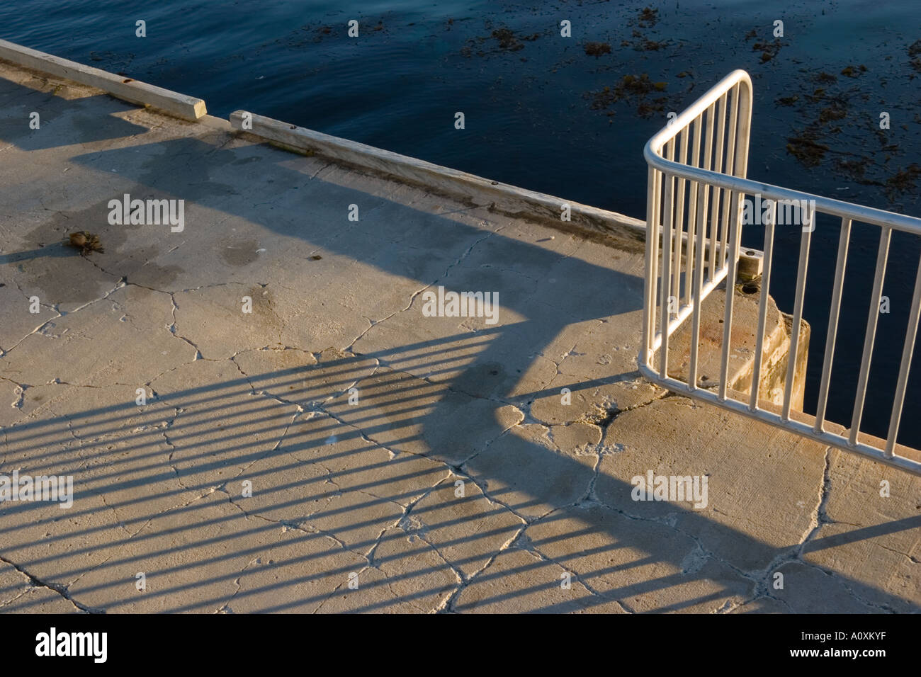 Garde-corps métallique avec ombre sur ciment fissuré avec de l'eau en arrière-plan Banque D'Images