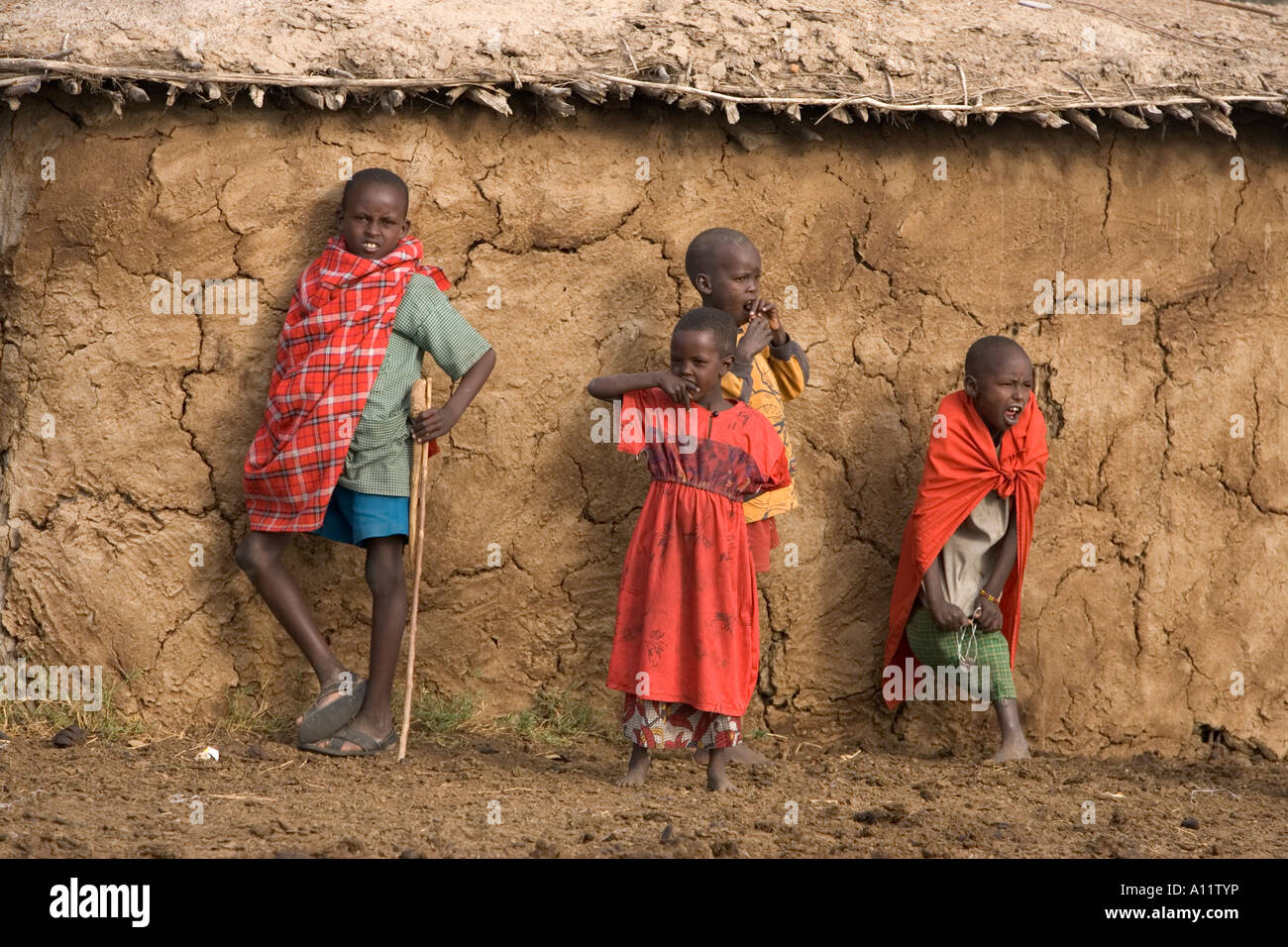 Frères et soeur Masaai posant devant leur hutte de terre dans leur village de Maasai Mara au Kenya Banque D'Images