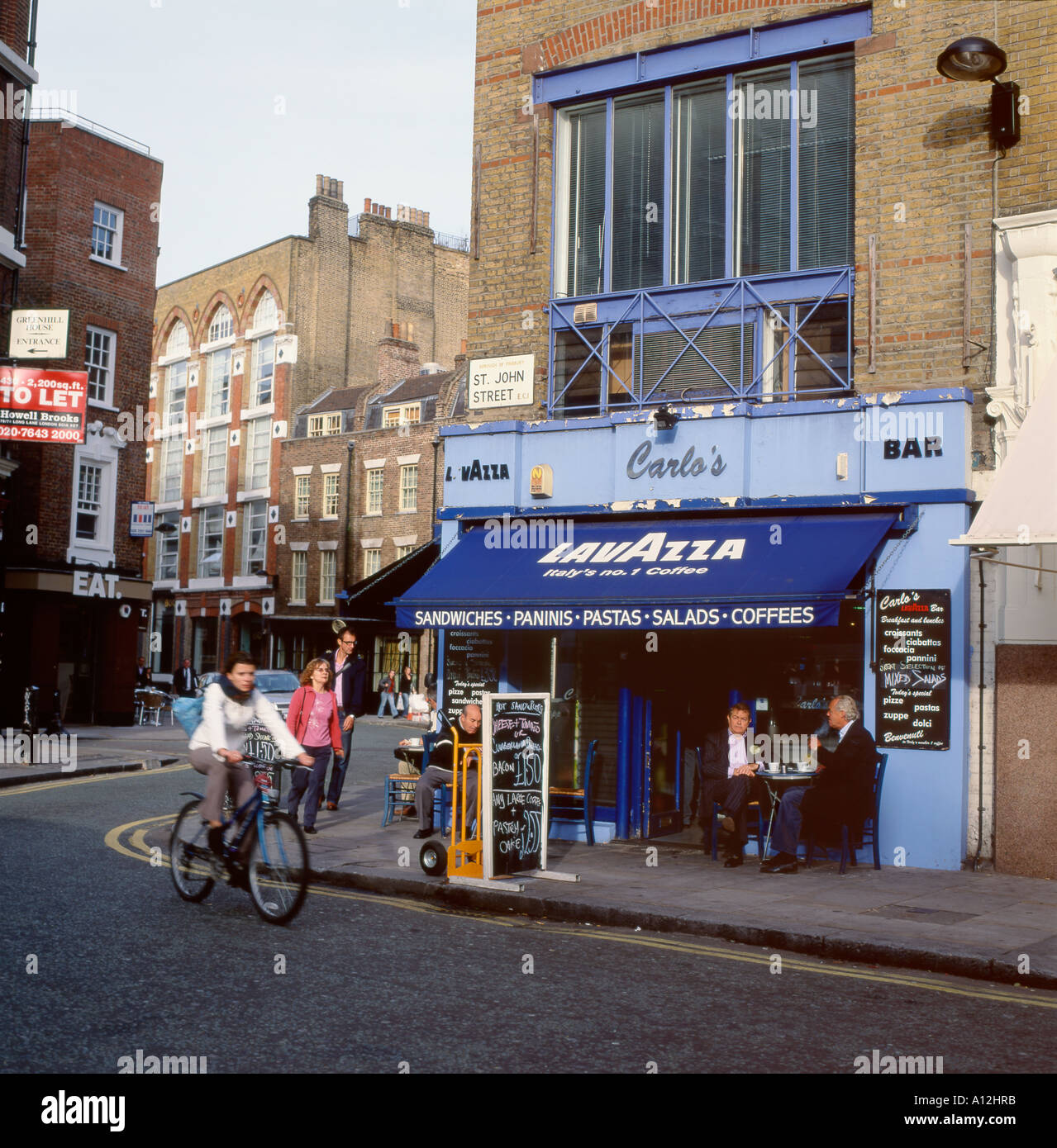 Woman riding son vélo passé Carlos bar café Lavazza à St John Street Clerkenwell Londres Angleterre Royaume-uni KATHY DEWITT Banque D'Images