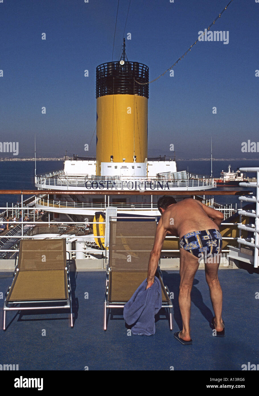 Homme de ramasser une serviette dans une chaise longue sur le pont supérieur d'un bateau Banque D'Images