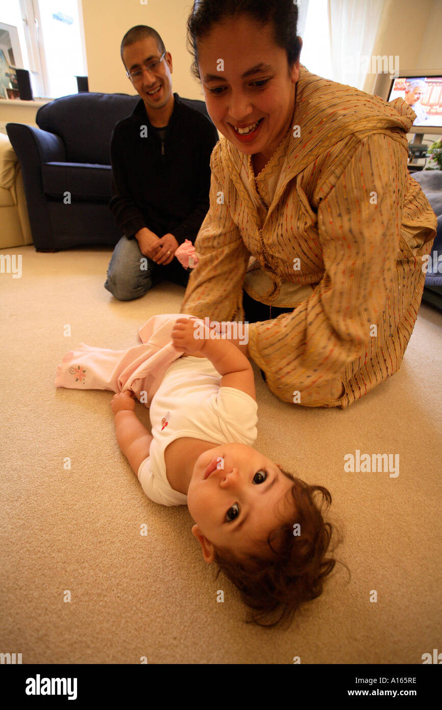 Portrait Couleur Vertical De Famille Marocaine En Angleterre Avec Bebe Fille Gisant Sur Le Sol Alors Que Sa Mere Change Ses Vetements Photo Stock Alamy