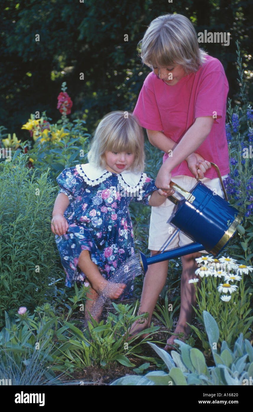 Deux jeunes filles, la famille, jouer avec un arrosoir bleu et nettoyer les pieds dans le jardin, Missouri USA Banque D'Images
