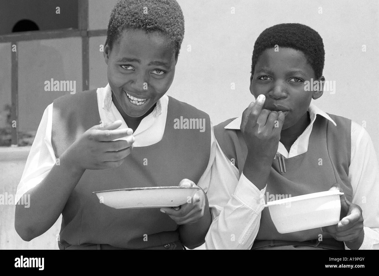 B/W de deux écolières rurales mangeant leur déjeuner financé par l'aide étrangère gratuite, leur seul repas quotidien dû à la sécheresse et à l'insécurité alimentaire.ESwatini, Swaziland Banque D'Images