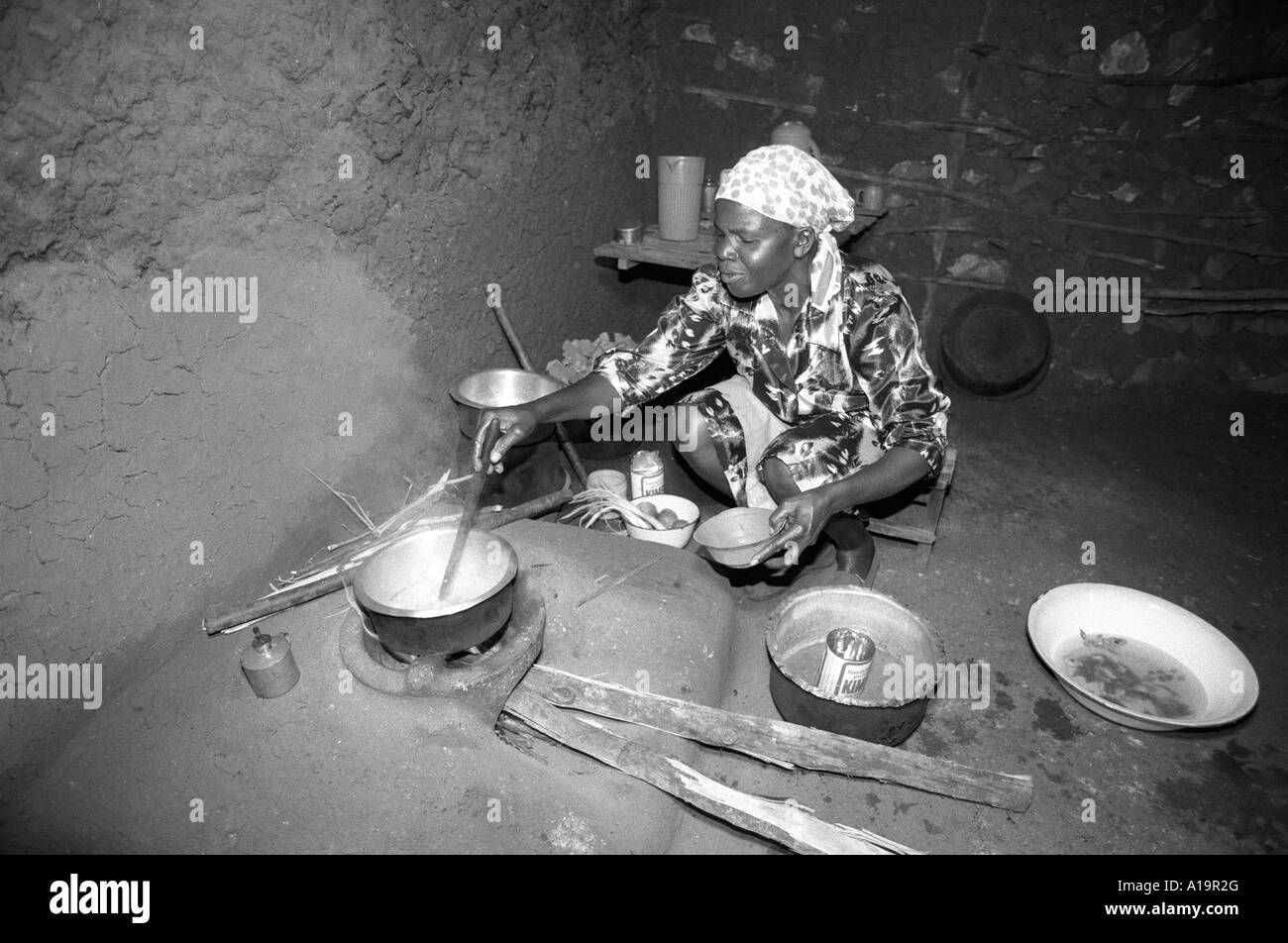 B/W d'une femme rurale à la maison cuisine sur un poêle amélioré, à faible consommation de carburant et écologique, fait par un groupe local de poterie pour femmes. Kisumu, Kenya Banque D'Images