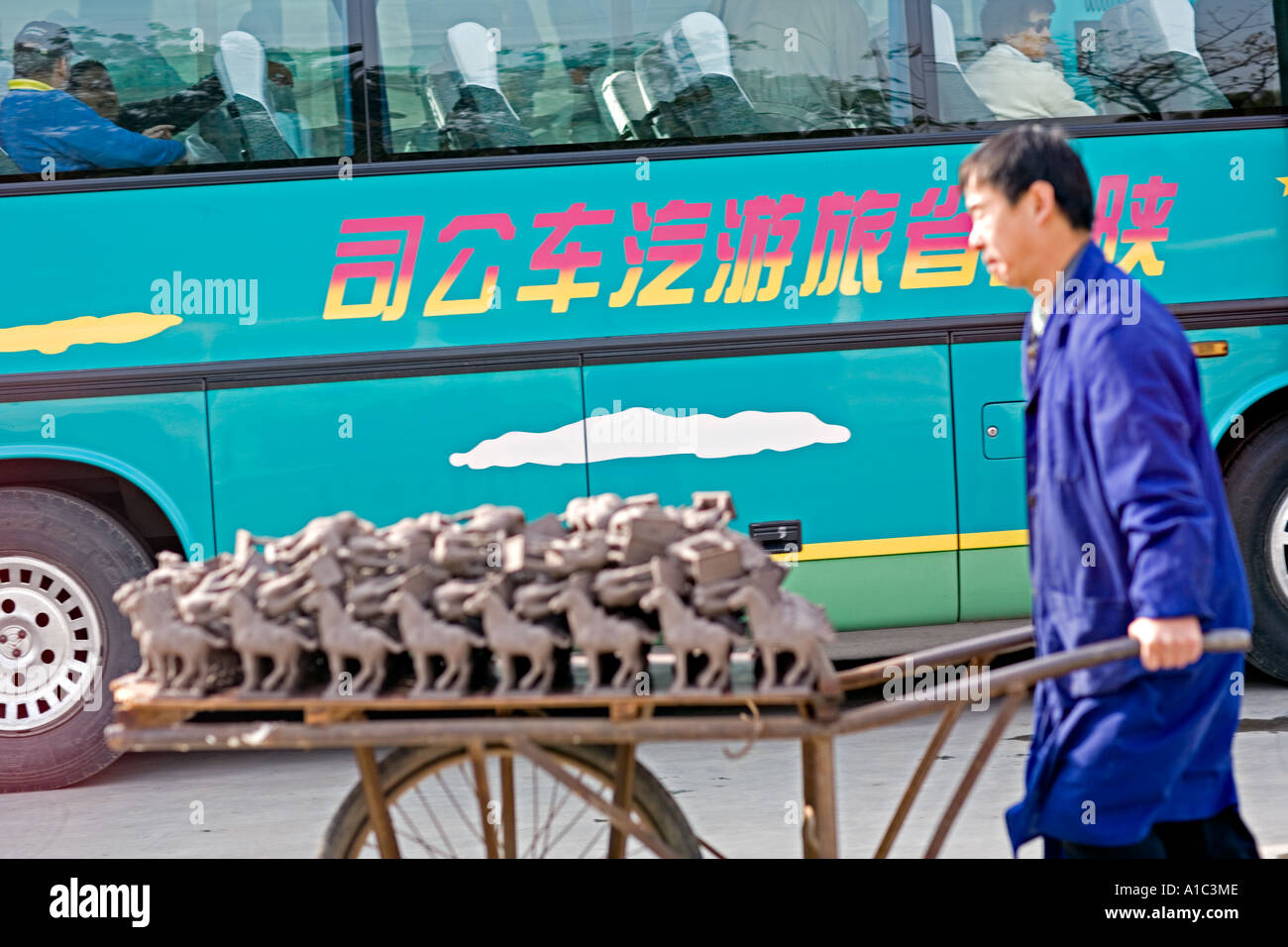 La CHINE XI'AN travailleur chinois pousse une brouette pleine de répliques des guerriers de terre cuite passé un tour bus chinois Banque D'Images