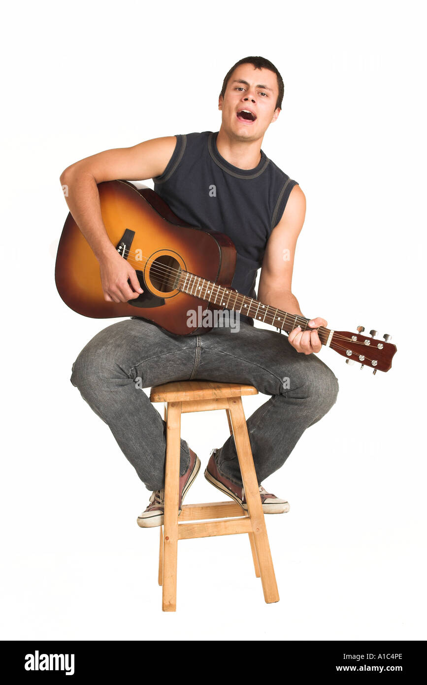 Jeune homme avec guitare assis sur une chaise en bois en chantant Banque D'Images