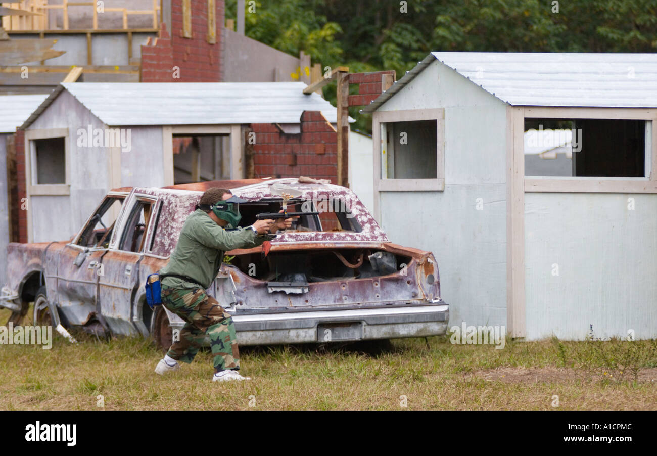 Jeune homme se cachant derrière l'équipe de tir à l'ennemi de voiture dans une partie de paintball Banque D'Images