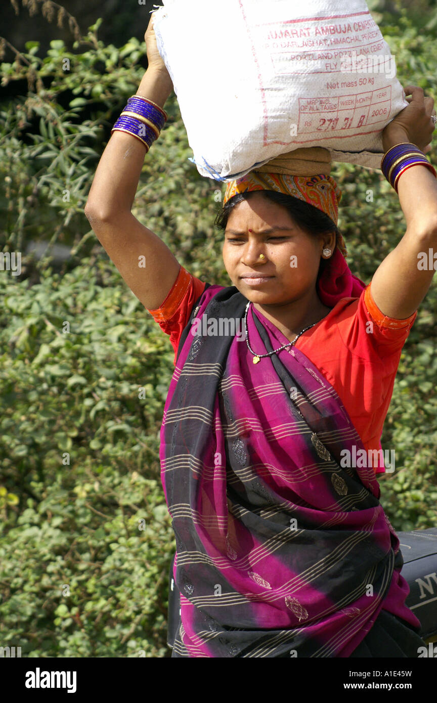 Vieille Femme indienne en sari coloré travaillant dur manuellement sur site de construction portant une charge lourde sur la tête Banque D'Images