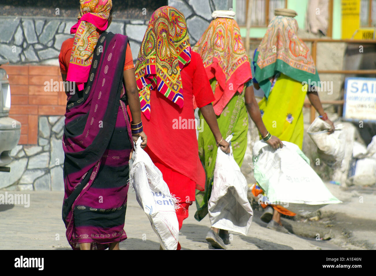Quatre de l'équipe femmes indiennes en sari coloré travaillant dur transportant des sacs de sable vide au site de construction de la rue, de l'Inde Banque D'Images