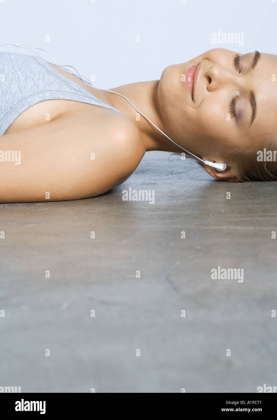 Woman lying on floor, listening to earphones Banque D'Images