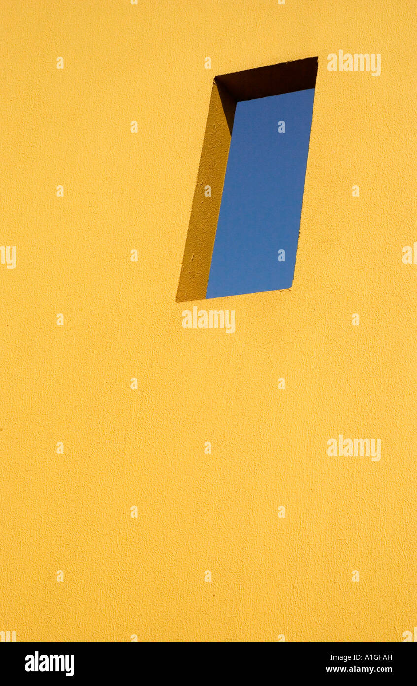 Ciel bleu profond à travers une fenêtre dans un mur en stuc jaune Banque D'Images