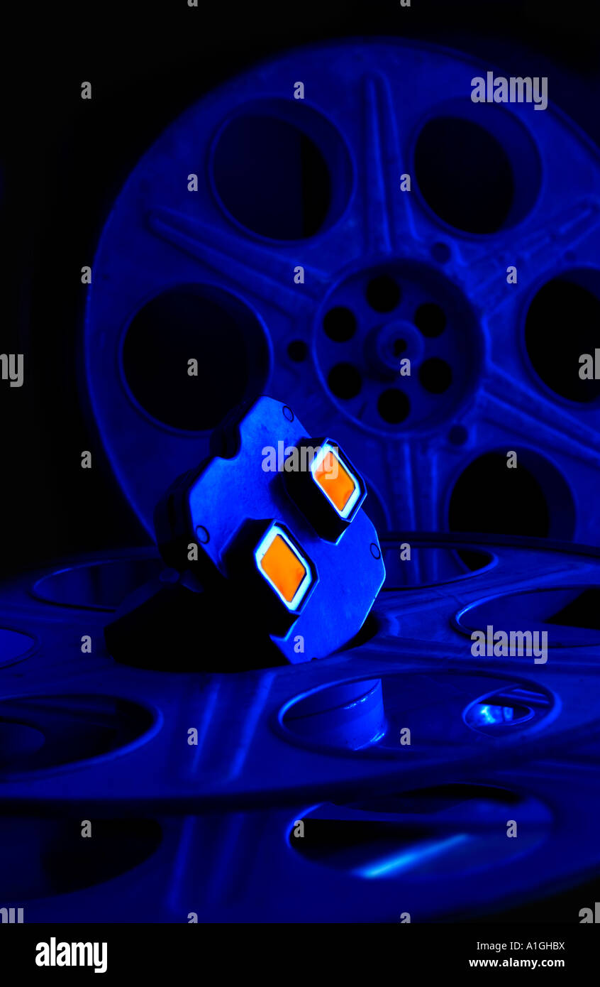 Un téléspectateur reflétant la lumière orange dans ses objectifs au sommet film film reels sont baignées de lumière d'un bleu profond. Banque D'Images