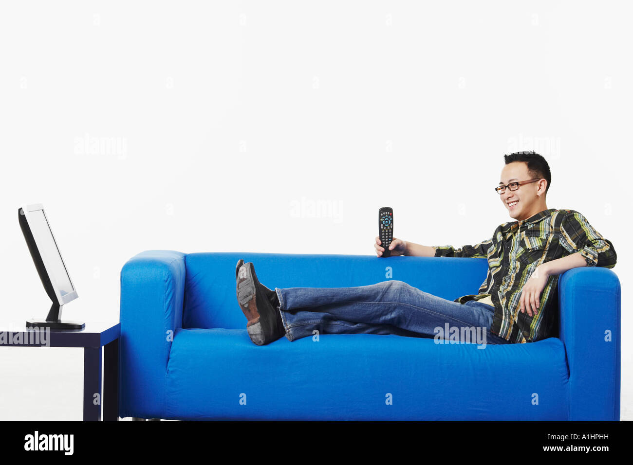 Portrait d'un jeune homme assis sur un canapé en regardant un écran plat Banque D'Images