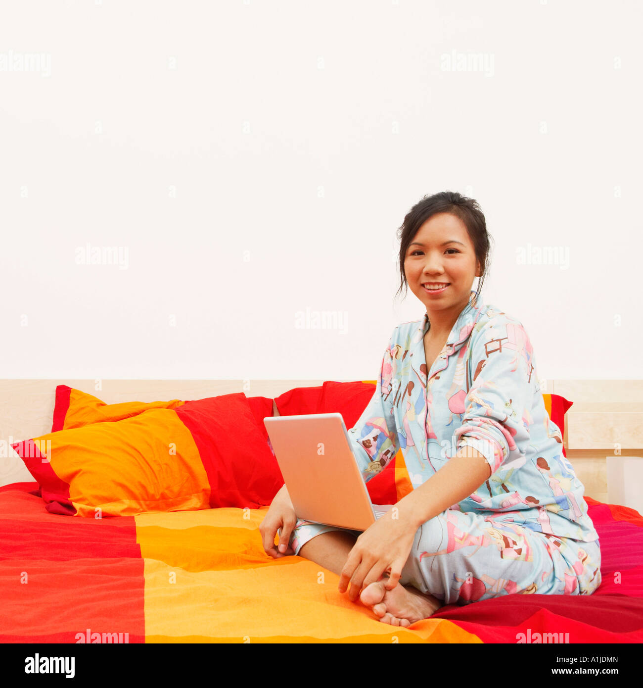 Portrait d'une jeune femme assise sur le lit avec un ordinateur portable et souriant Banque D'Images