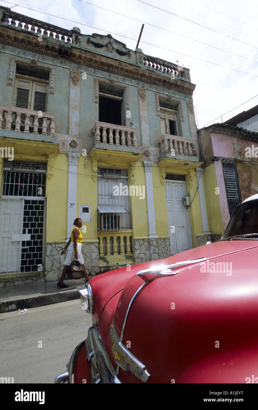 Frontside d'une vieille Chevrolet rouge garée dans une rue bordée de maisons jaunes. Banque D'Images