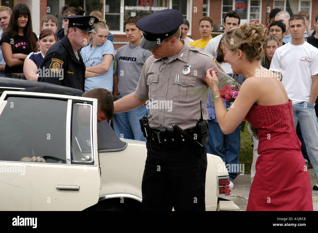 Prom Drunk Driving Demo policier aide les passagers à l'arrière de la voiture tandis que les filles en détresse cherche sur les adolescents Banque D'Images