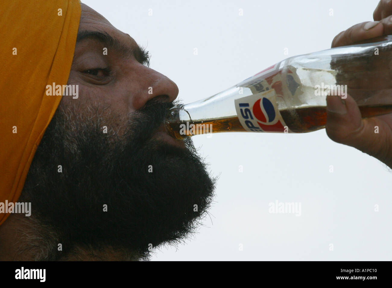 Un sikh portant un turban boissons à partir d'une bouteille de cola persi à New Delhi en Inde. Banque D'Images