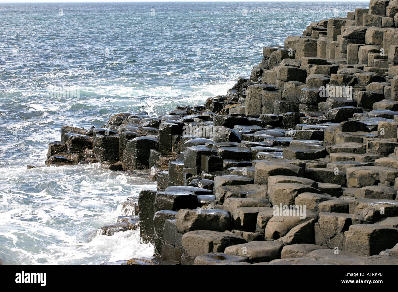 Stepping Stones hexagonal : le noir basalte hexagonal de la Chaussée des géants l'étape jusqu'à une mer bleu clair d'ébullition Banque D'Images