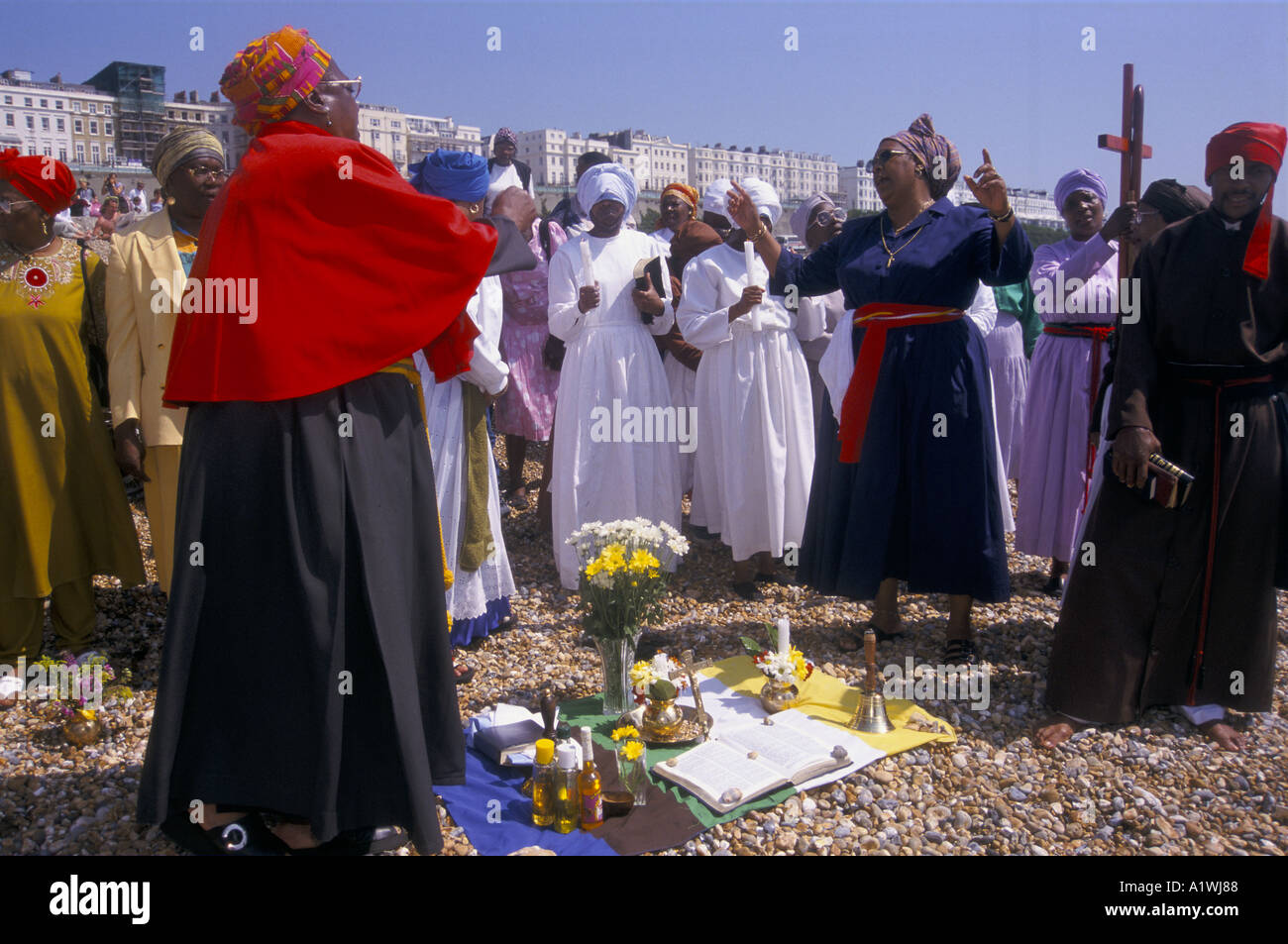 Cérémonie de baptême chrétien DANS LA MER À BRIGHTON LES GENS vêtus de robes colorées SE RASSEMBLENT SUR LA PLAGE Banque D'Images