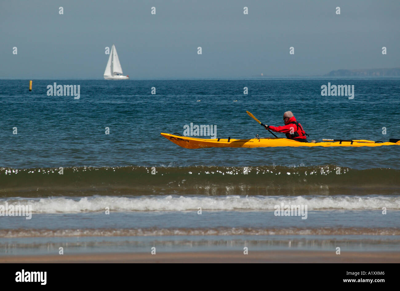 Canoe jaune avec l'homme l'aviron en veste rouge à proximité de la côte écossaise avec location dans l'arrière-plan Banque D'Images