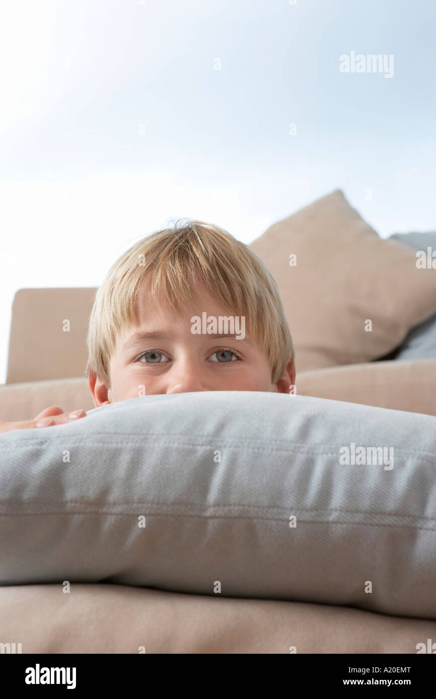 Jeune garçon se cachant derrière les coussins et oreillers Banque D'Images