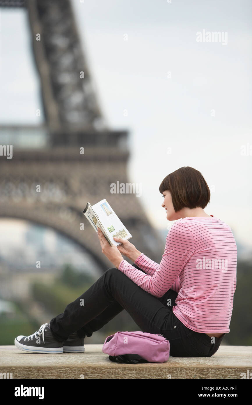 France, Paris, young woman reading book sur balcon en face de la Tour Eiffel Banque D'Images