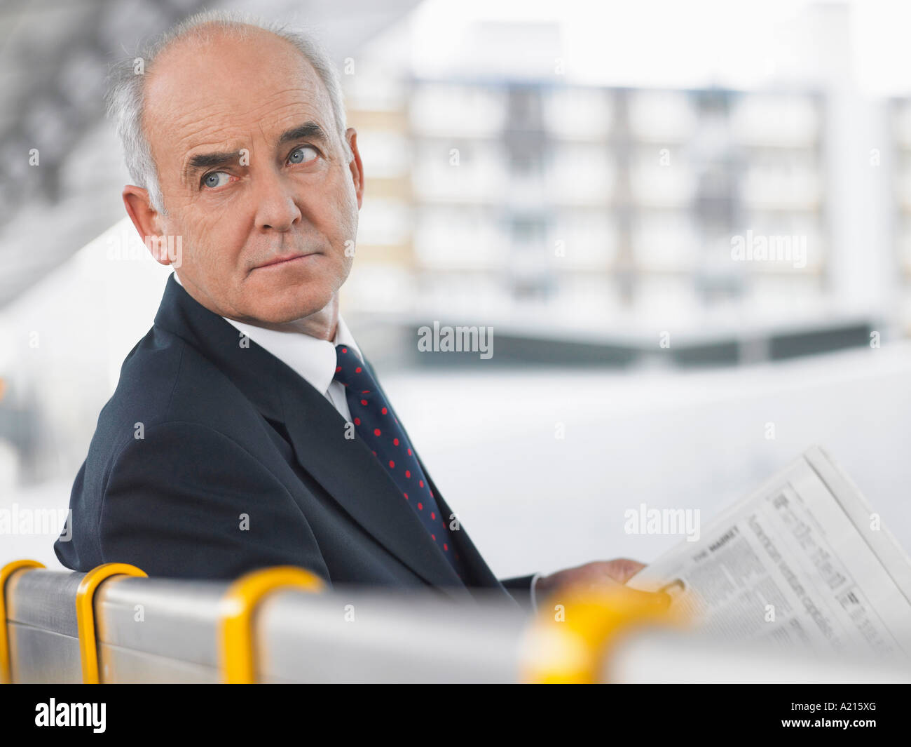 Mature Businessman Sitting on Bench avec journal, looking over shoulder Banque D'Images
