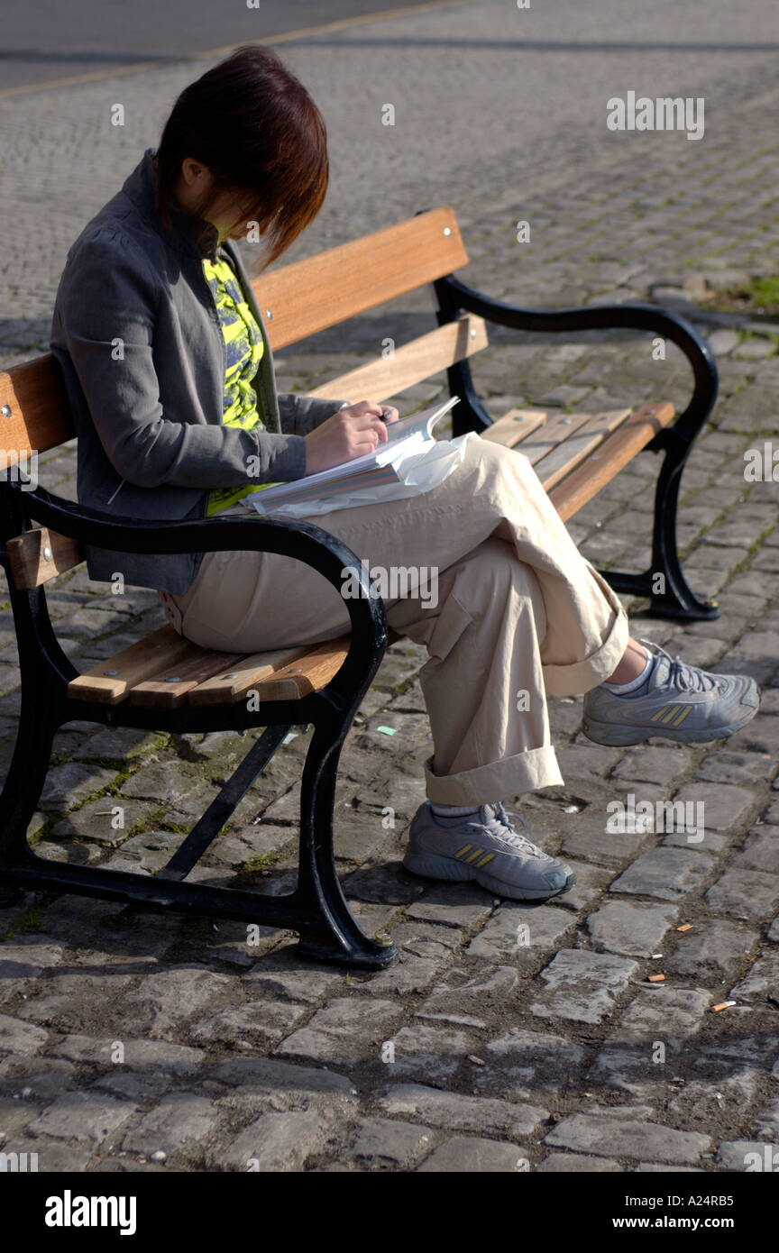 Femme assise toute seule sur banc de parc la lecture avec sa tête en bas Banque D'Images