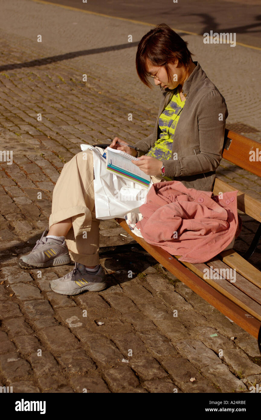 Femme assise toute seule sur banc de parc la lecture avec sa tête en bas Banque D'Images
