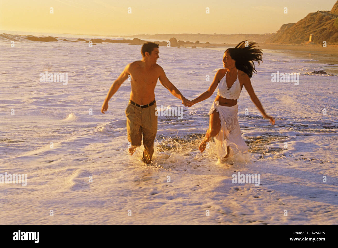 Couple heureux moments romantiques dans des vagues se brisant sur la côte de sable le long de la côte sud de la Californie au coucher du soleil Banque D'Images