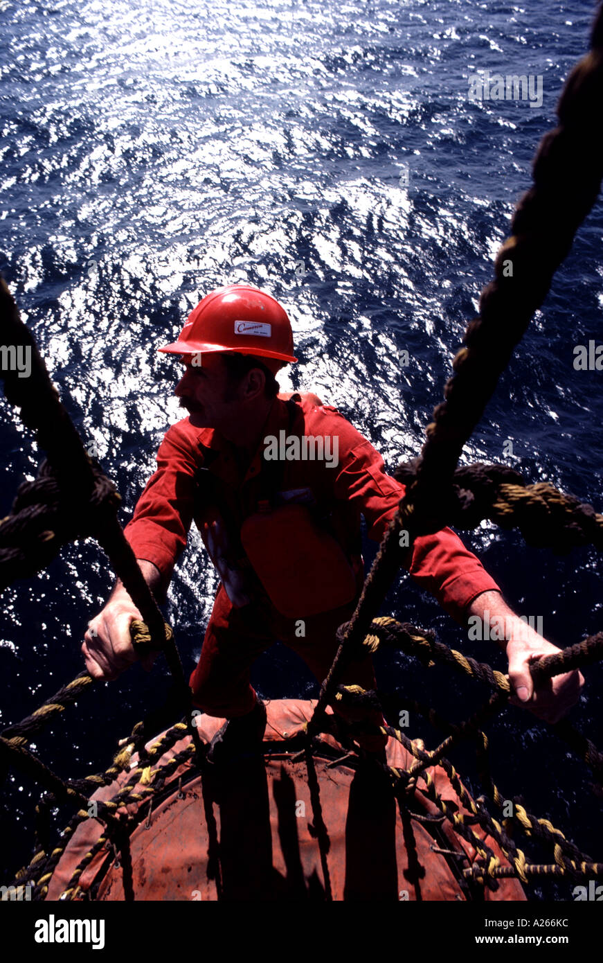 Un travailleur de l'industrie pétrolière regards sur l'horizon alors qu'il effectue des réparations suspendue au-dessus d'une plate-forme off-shore. Banque D'Images