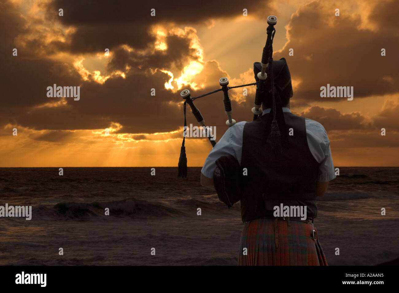 Le dirigeant d'une cornemuse joue sa chanson triste en face d'un merveilleux coucher de soleil de l'océan. Banque D'Images
