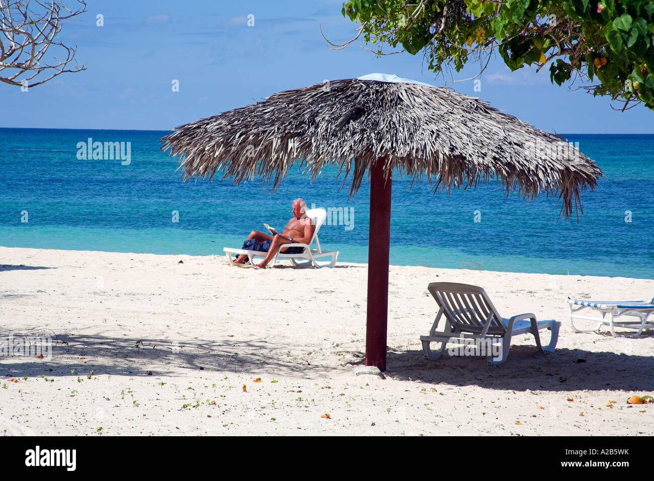 Détente homme près d'un parasol sur une plage, Guardalavaca, Holguin, Cuba Province Banque D'Images