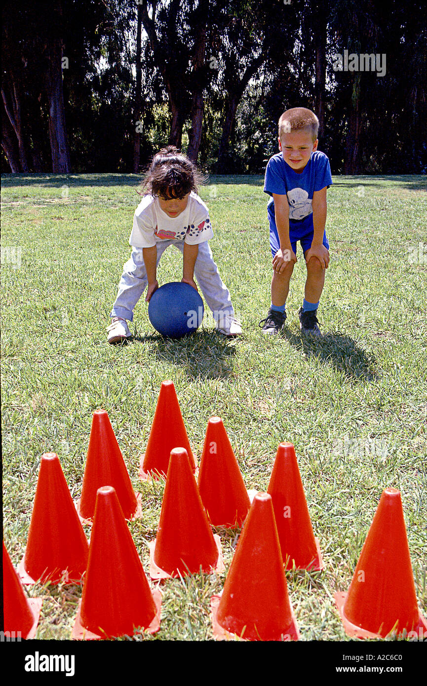 Deux enfants 5-7 ans garçon fille jouant à l'extérieur coopérative POV kiddies lawn bowling rolling ball diversité raciale ethnique diverses cibles Banque D'Images