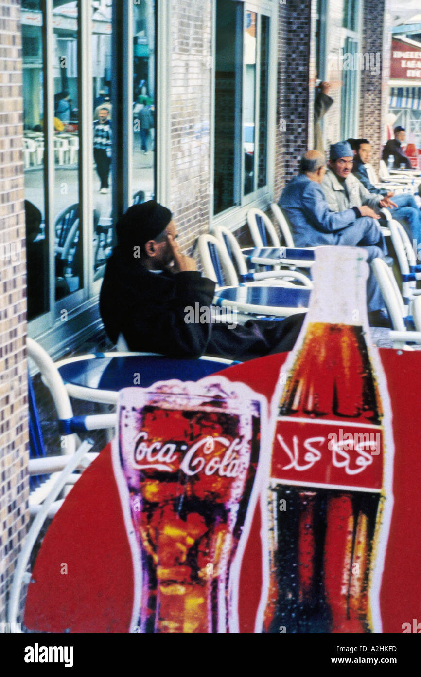 Afrique Maroc Tanger hommes marocain assis à la terrasse d'un café qui affiche une publicité pour Coca Cola en Arabe Banque D'Images