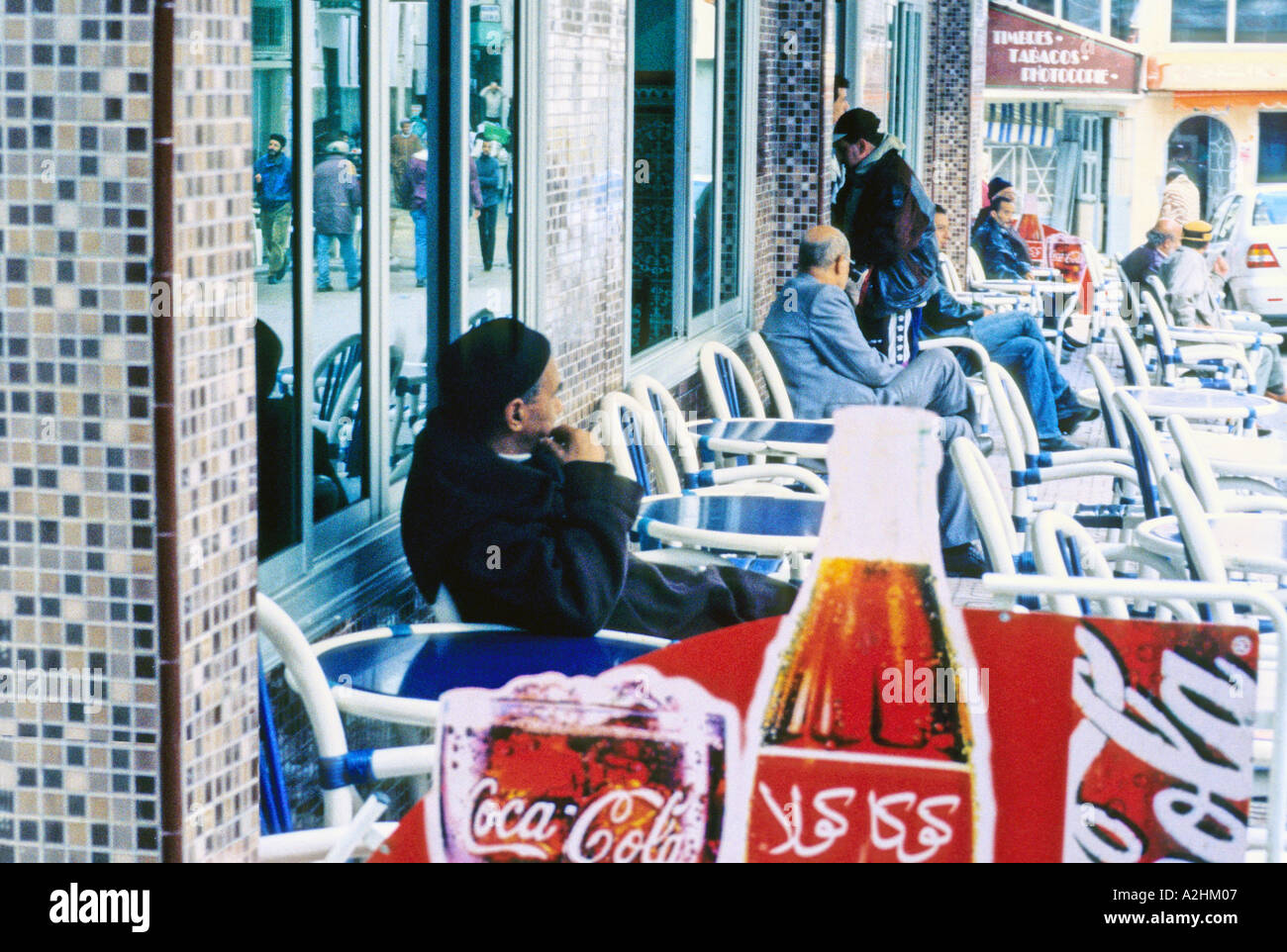 Afrique Maroc Tanger hommes marocain assis à la terrasse d'un café qui affiche une publicité pour Coca Cola en Arabe Banque D'Images
